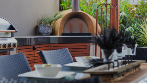 A nice outdoor kitchen with a woodfire stove and ample counterspace as well as a dining table.